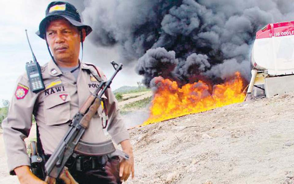 Indonesian police officer stands in front of oil fire in Aceh (Tribune)