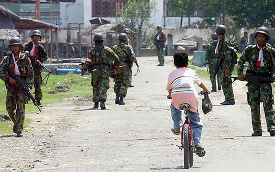 Child rides bike past Indonesian soldiers in Aceh (Tirto)