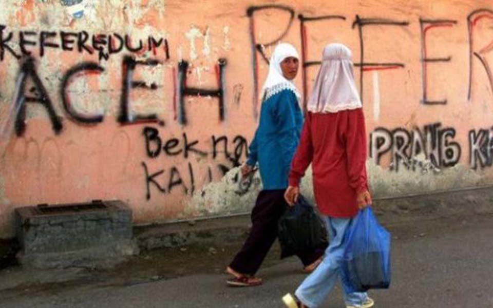 Women walk past graffiti calling for independence referendum in Aceh (Arif Agung Prasetyo)